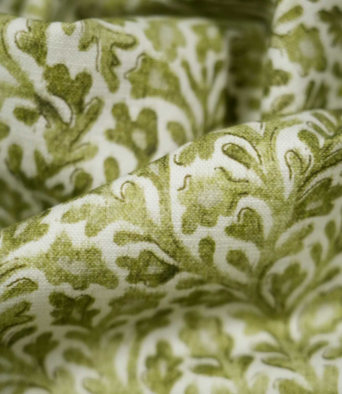 Detailed close-up of draped Elmsley Green fabric, highlighting the woven surface texture, softly printed olive and moss green leaves, stylised flowers and flowing foliage pattern against a warm off-white ground.