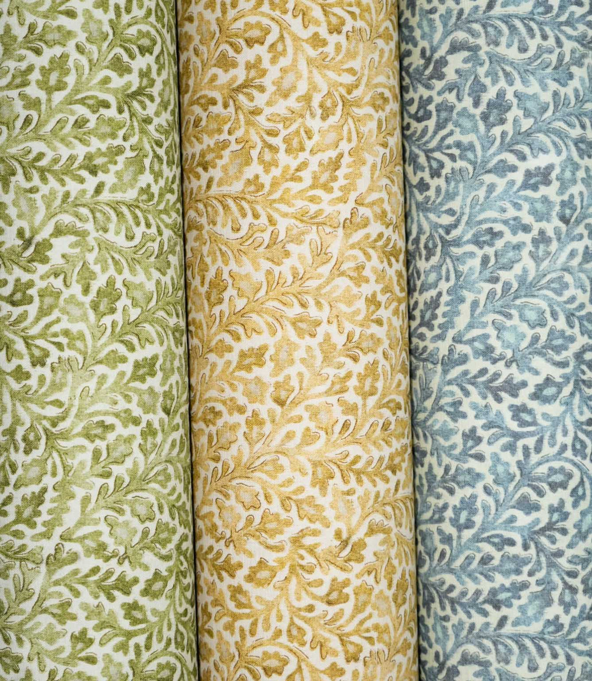 Three Elmsley floral fabrics displayed side by side in green, ochre and blue colourways, each featuring the same small-scale flowing foliage and stylised floral pattern on a soft off-white ground.