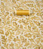 Elmsley Ochre floral fabric displayed with a coordinating golden ochre thread spool, highlighting the tonal botanical print, small-scale foliage design and softly textured fabric surface against a warm off-white ground.