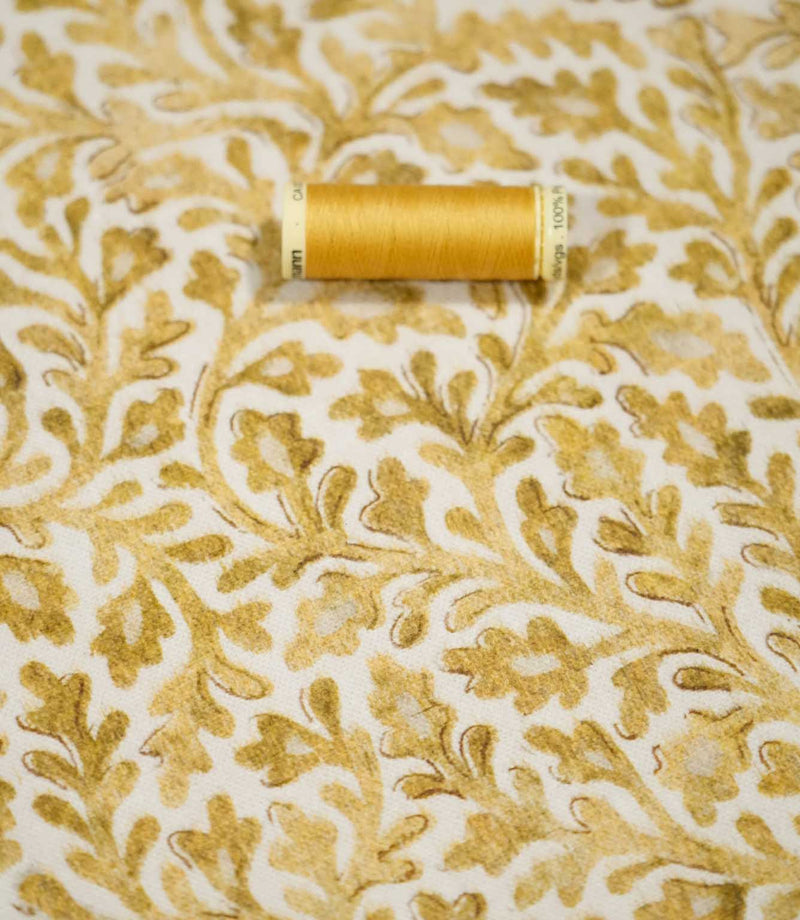 Elmsley Ochre floral fabric displayed with a coordinating golden ochre thread spool, highlighting the tonal botanical print, small-scale foliage design and softly textured fabric surface against a warm off-white ground.