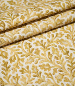 Elmsley Ochre fabric arranged in neat layered folds, displaying the repeating small-scale floral and foliage pattern, softly printed golden ochre tones and subtle woven surface texture on a warm off-white ground.