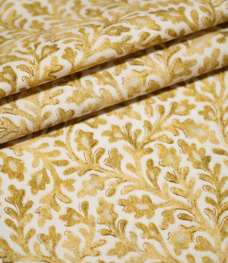 Elmsley Ochre fabric arranged in neat layered folds, displaying the repeating small-scale floral and foliage pattern, softly printed golden ochre tones and subtle woven surface texture on a warm off-white ground.