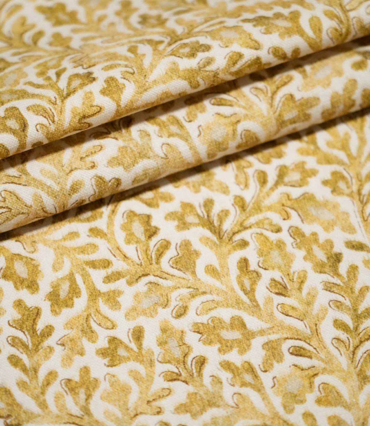 Elmsley Ochre fabric arranged in neat layered folds, displaying the repeating small-scale floral and foliage pattern, softly printed golden ochre tones and subtle woven surface texture on a warm off-white ground.