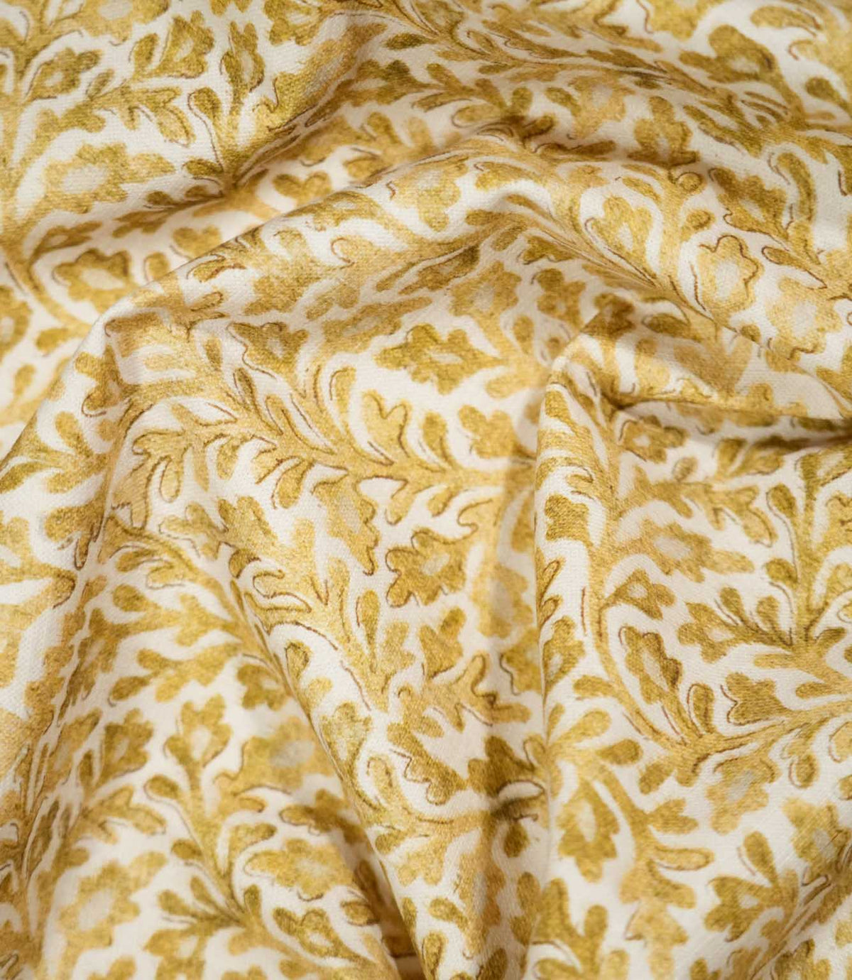 Elmsley Ochre fabric loosely draped into soft, flowing folds, showing the movement and scale of its intricate botanical design with warm golden ochre leaves, stems and stylised flowers across an off-white ground.