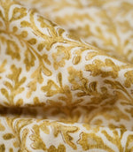 Macro detail of Elmsley Ochre fabric gathered into soft folds, highlighting the woven texture and hand-rendered botanical print of golden ochre foliage, delicate floral shapes and fine darker outlines on an off-white ground.