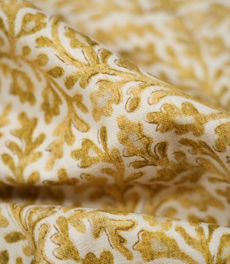 Macro detail of Elmsley Ochre fabric gathered into soft folds, highlighting the woven texture and hand-rendered botanical print of golden ochre foliage, delicate floral shapes and fine darker outlines on an off-white ground.