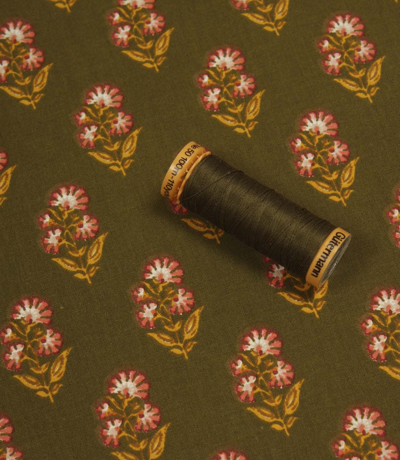 Olive floral print fabric displayed with a coordinating dark thread spool to highlight colour matching.