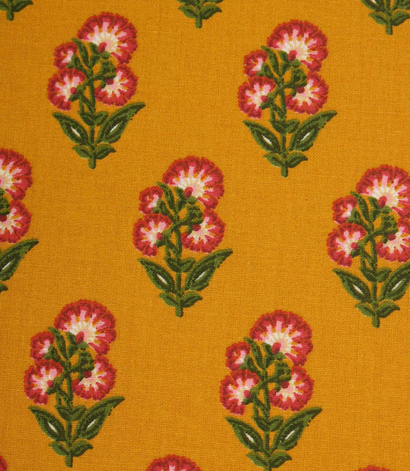 Close-up of mustard floral fabric with small stylised flower motifs in pink, white, and green on a warm golden background.
