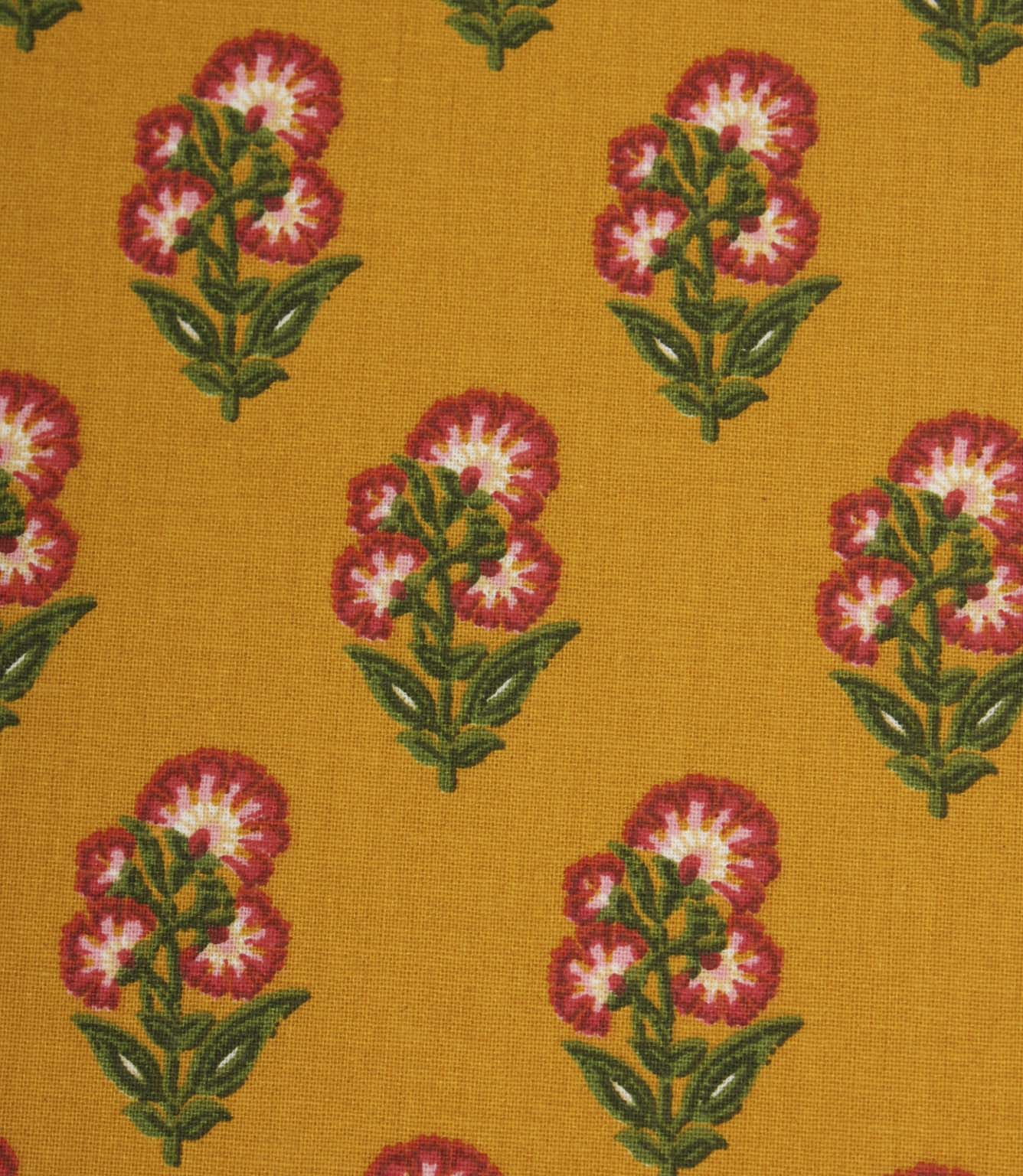 Close-up of mustard floral fabric with small stylised flower motifs in pink, white, and green on a warm golden background.