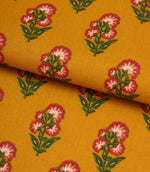 Mustard botanical print fabric folded to show the smooth texture and repeating floral design.