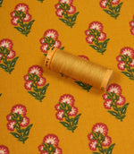 Floral print fabric in mustard yellow shown with a matching thread spool, featuring pink flower motifs and green leaves.