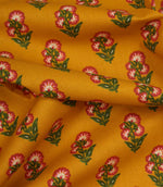 Draped mustard cotton fabric with repeating pink floral sprigs and soft green foliage detail.