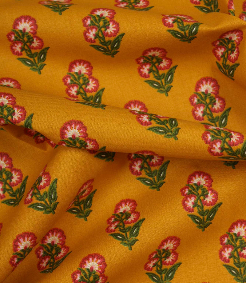 Draped mustard cotton fabric with repeating pink floral sprigs and soft green foliage detail.