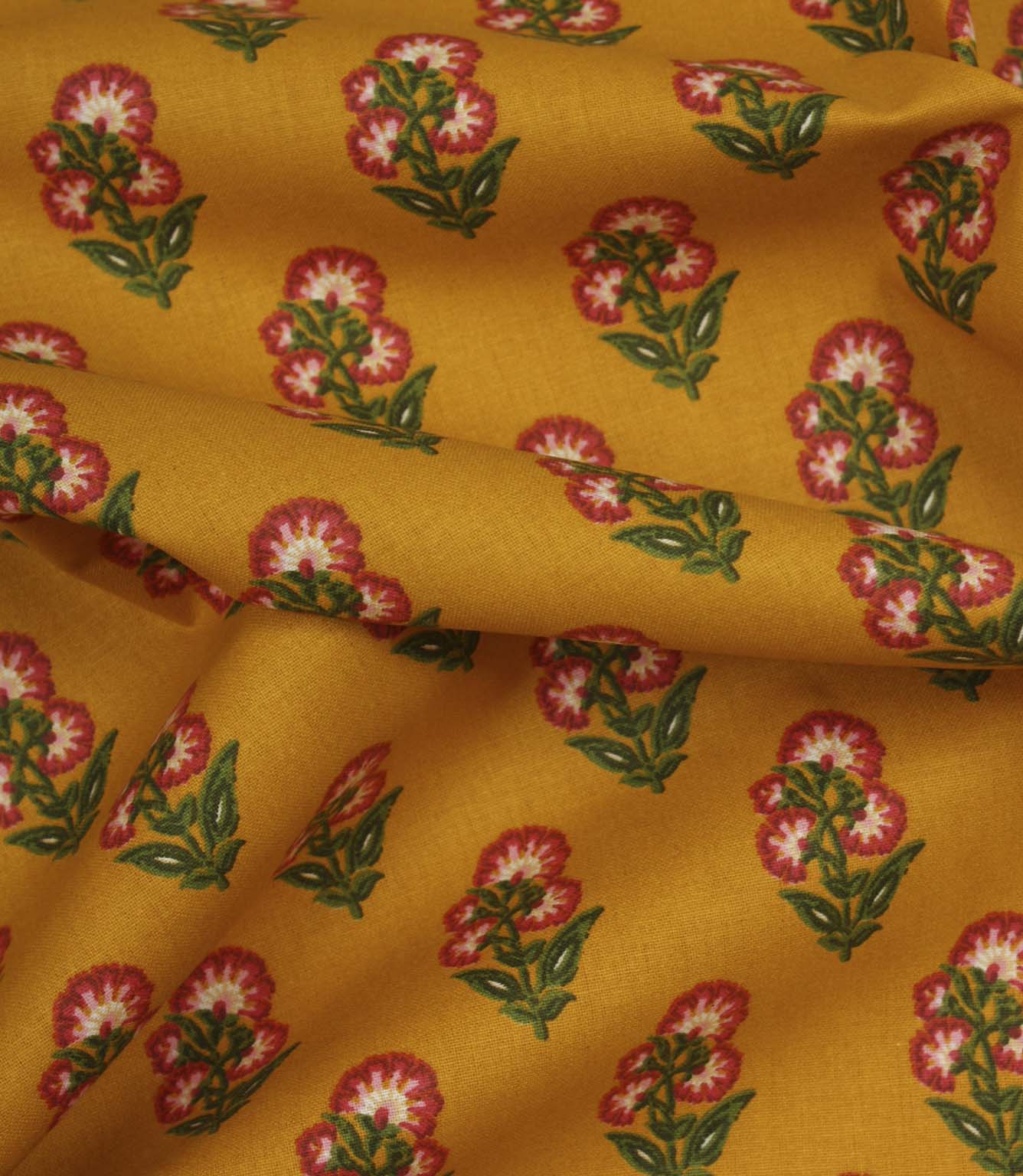 Draped mustard cotton fabric with repeating pink floral sprigs and soft green foliage detail.