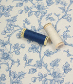 Floral vine fabric displayed with coordinating blue and ivory thread spools to highlight colour matching options.