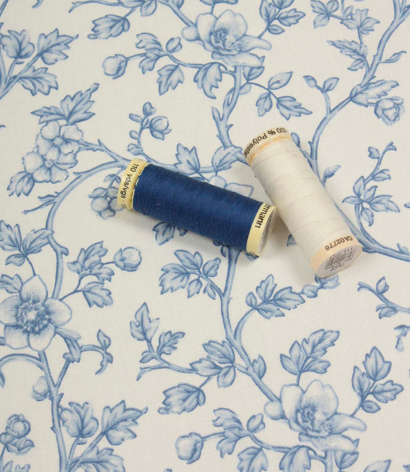 Floral vine fabric displayed with coordinating blue and ivory thread spools to highlight colour matching options.