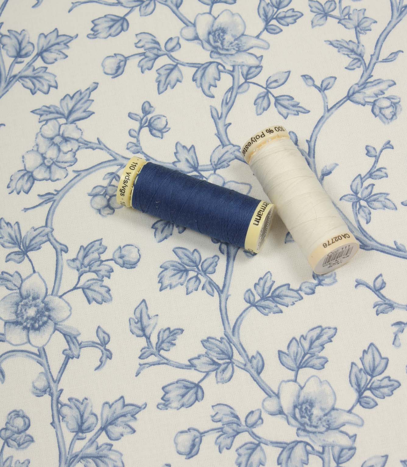 Floral vine fabric displayed with coordinating blue and ivory thread spools to highlight colour matching options.