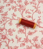Red floral fabric laid flat with a coordinating spool of red thread, highlighting the elegant botanical print and soft woven finish.