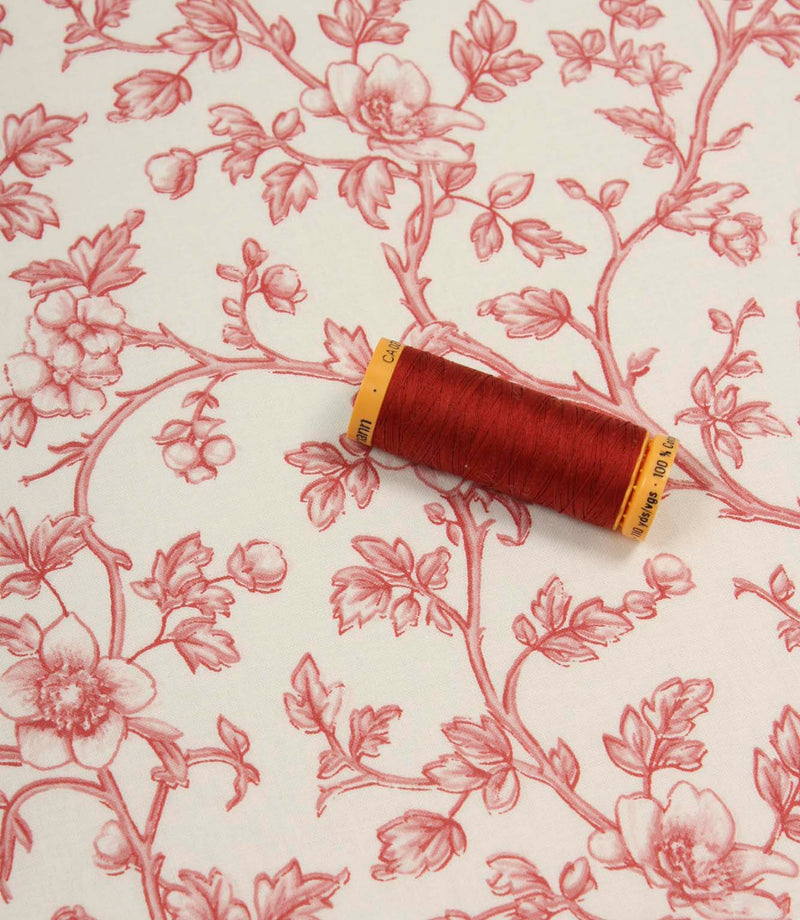 Red floral fabric laid flat with a coordinating spool of red thread, highlighting the elegant botanical print and soft woven finish.