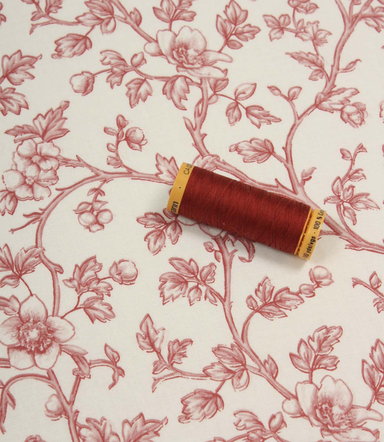 Red floral fabric laid flat with a coordinating spool of red thread, highlighting the elegant botanical print and soft woven finish.