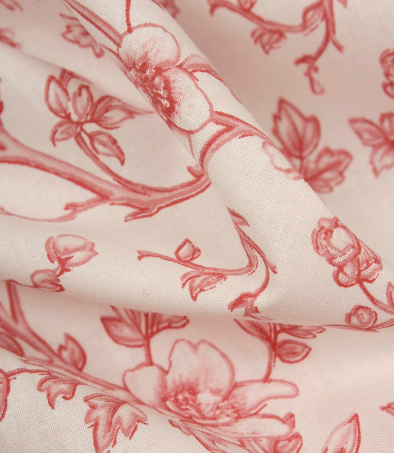 Detailed close-up of folded floral fabric revealing the fine weave, soft handle, and delicate red botanical design on an ivory background.