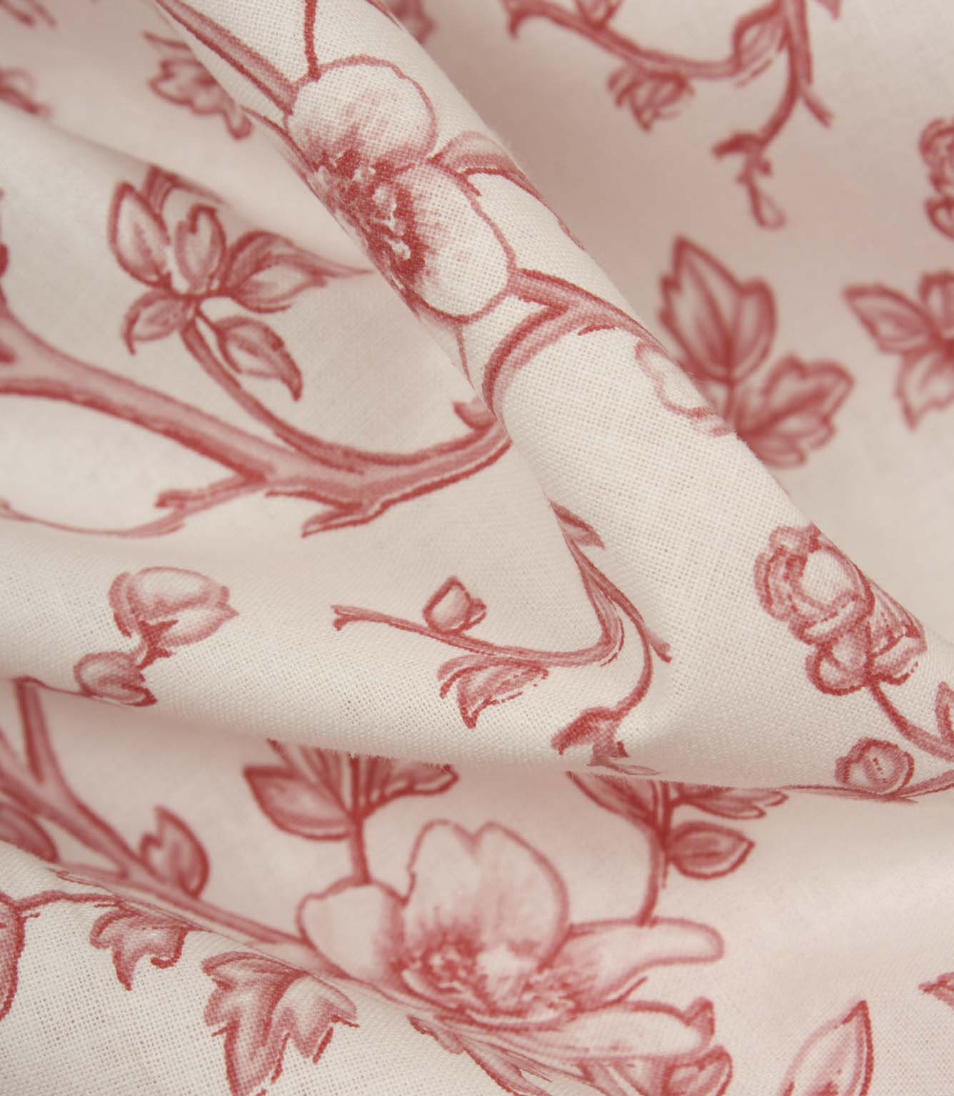 Detailed close-up of folded floral fabric revealing the fine weave, soft handle, and delicate red botanical design on an ivory background.