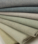 Stack of folded herringbone fabric in various shades of green and blue.