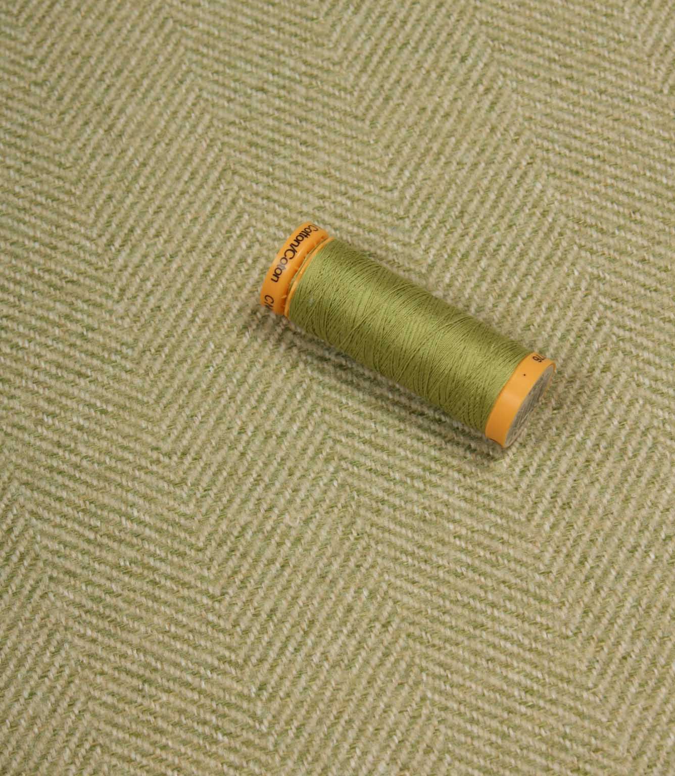 Green spool of thread on a textured fabric background