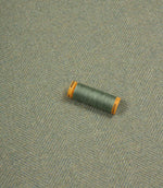 Green spool of thread on a textured blue fabric background
