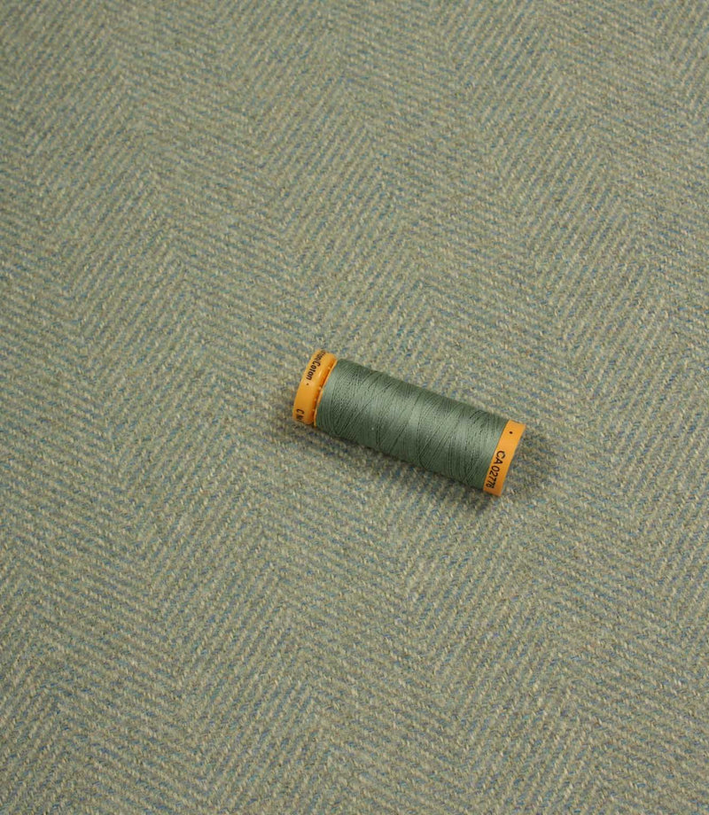 Green spool of thread on a textured blue fabric background