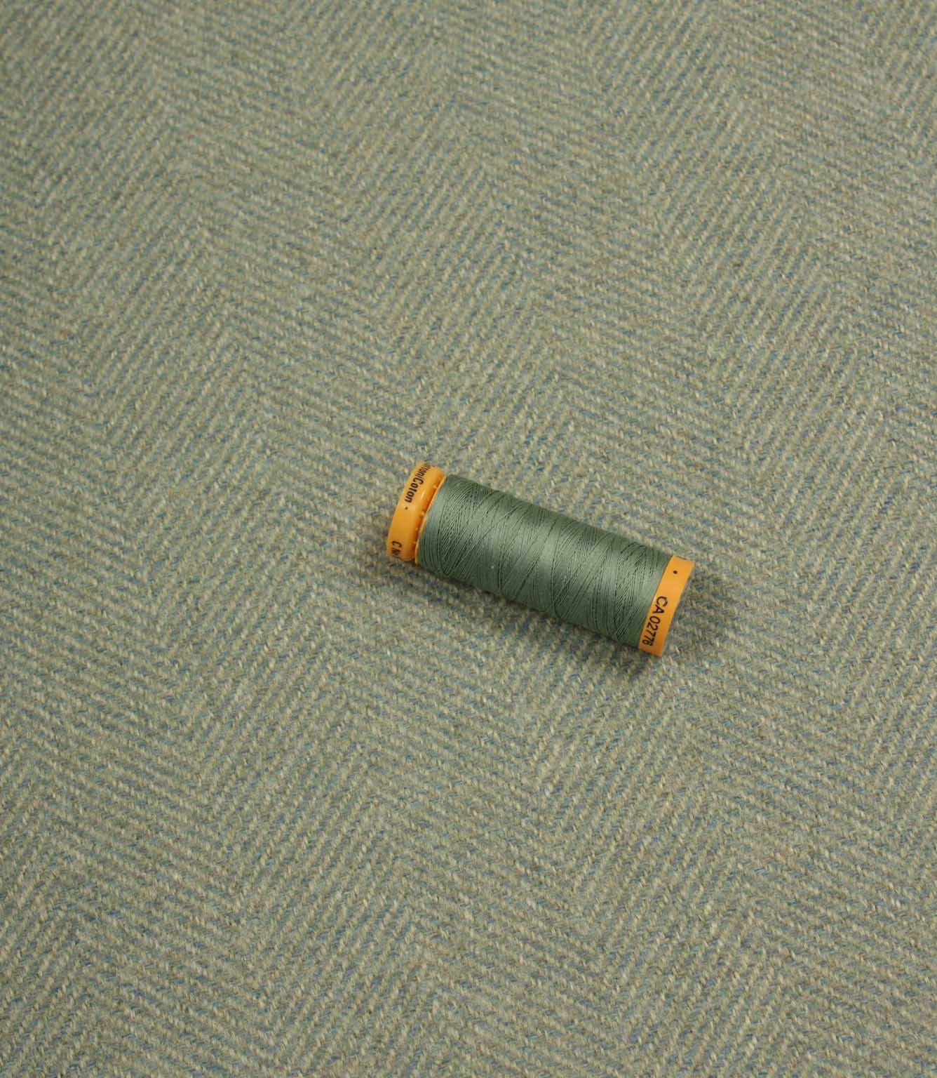 Green spool of thread on a textured blue fabric background