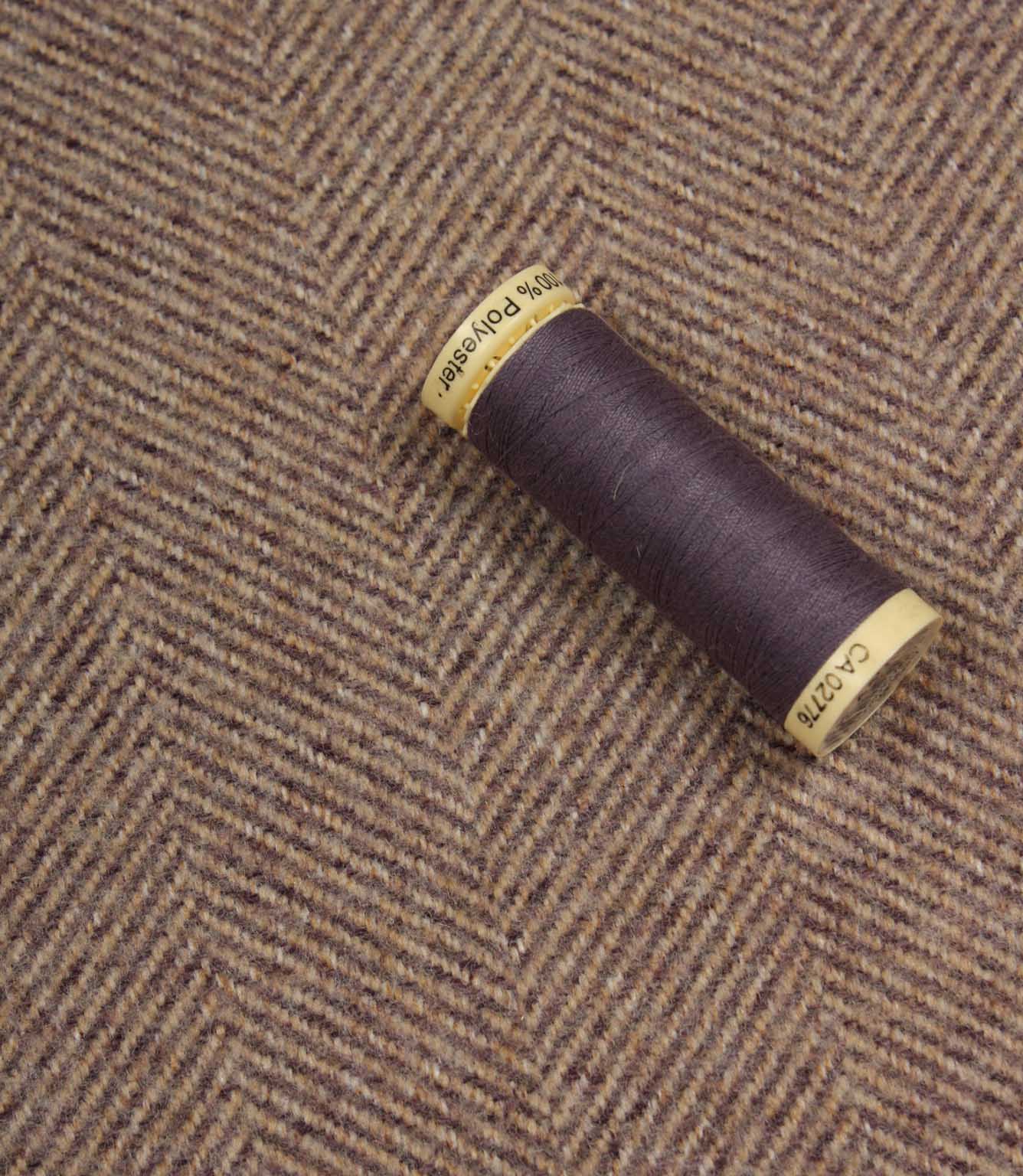 Spool of purple thread on a textured lavender fabric background