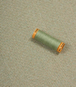 Spool of green thread on a textured fabric background