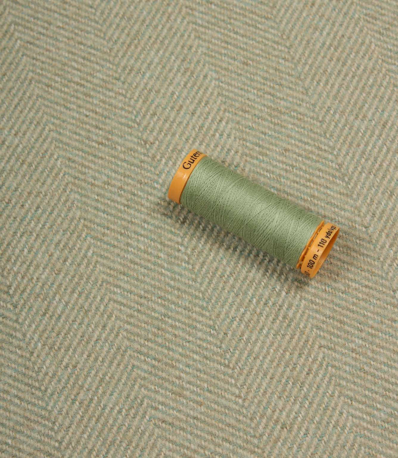 Spool of green thread on a textured fabric background