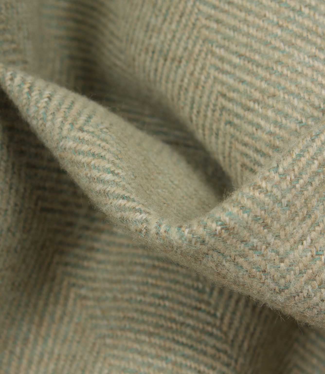 Close-up of a textured fabric with a herringbone pattern in green and beige.