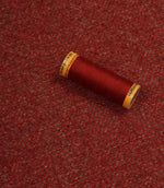 Spool of red thread on a textured red fabric background