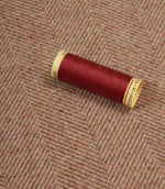 Red spool of thread on a textured rose fabric background