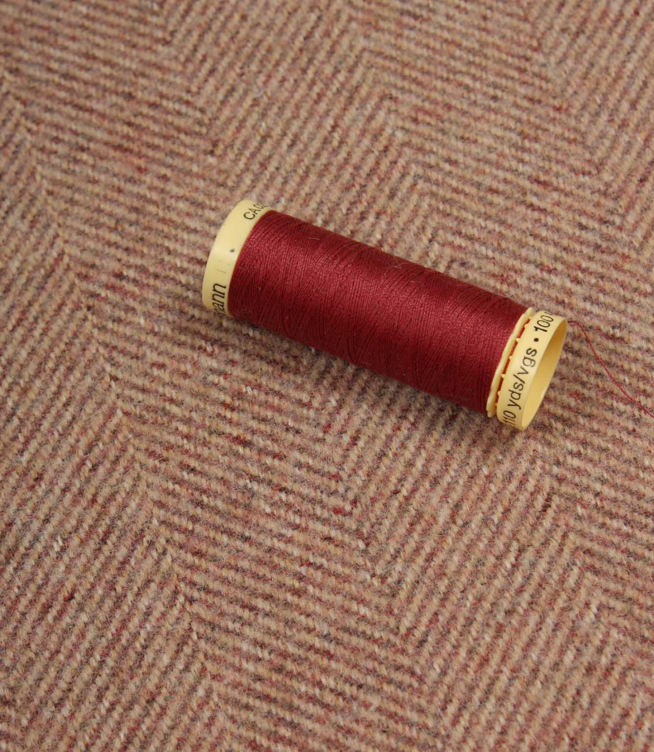 Red spool of thread on a textured rose fabric background
