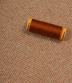 Spool of brown thread on a textured fabric background