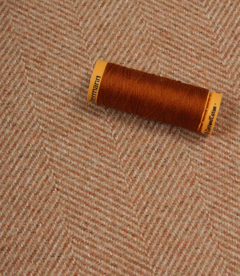 Spool of brown thread on a textured fabric background