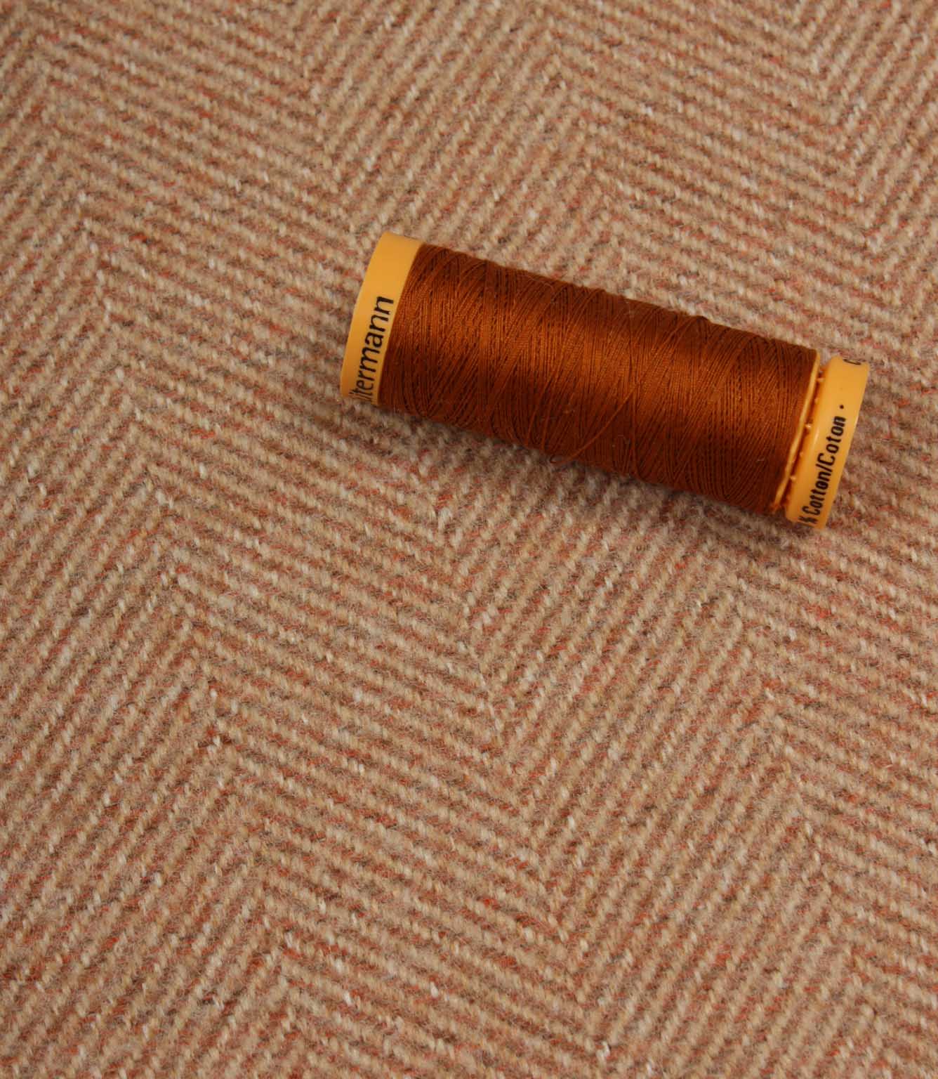 Spool of brown thread on a textured fabric background