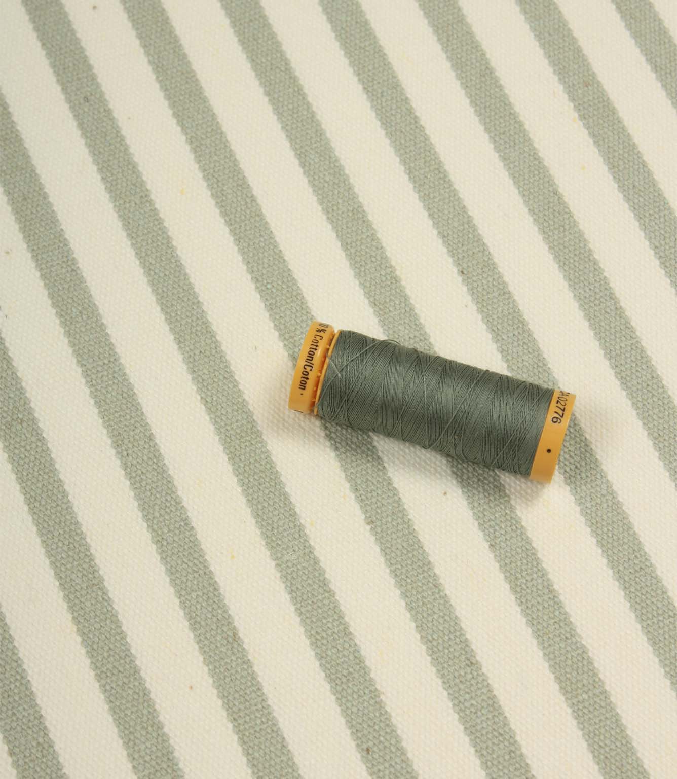 Fernley Stripe sage green striped upholstery fire retardant fabric displayed with matching thread to showcase colour coordination and woven texture.