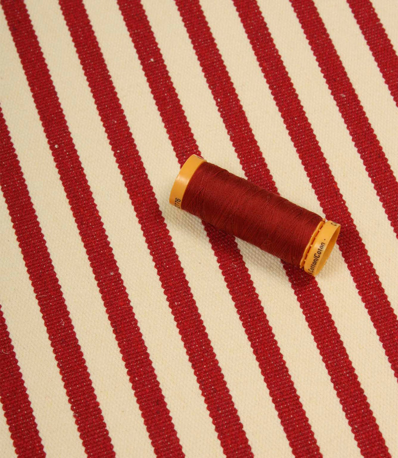 Fernley Stripe wine red stripe upholstery fabric displayed with matching thread, highlighting colour coordination and woven texture.