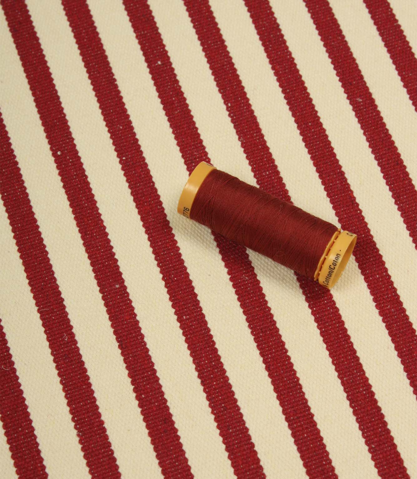 Fernley Stripe wine red stripe upholstery fabric displayed with matching thread, highlighting colour coordination and woven texture.