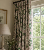 Patterned green and beige curtain hanging in a room with a lamp and window.