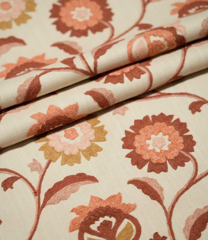 Foxmere Burnt Sienna fabric arranged in soft folds, displaying the flowing embroidered vine pattern with large stylised flowers, leaves and buds in earthy burnt sienna, terracotta, blush pink and ochre tones.