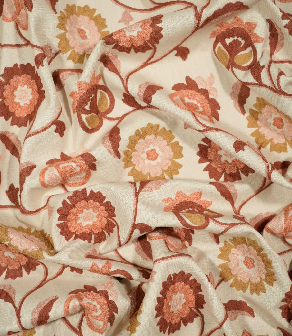Foxmere Burnt Sienna embroidered fabric loosely draped to show its texture and handle, with a repeating botanical design of winding stems, leaves and decorative flowers across a natural cream woven background.