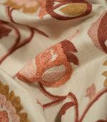 Macro close-up of Foxmere Burnt Sienna fabric, revealing the detailed raised embroidery and individual stitches forming a stylised flower bud in terracotta, burnt sienna, blush pink and ochre on a textured natural cream base.