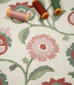 Detailed view of Foxmere Chintz floral fabric with coordinating pink, red and green thread spools resting above the design, highlighting the colours and textured embroidery of the flowers, leaves and trailing stems.