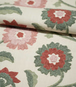 Foxmere Chintz embroidered floral fabric folded over itself, showing the tactile raised stitching and woven cream ground, with layered dusty pink and soft red flowers surrounded by contrasting sage and deeper green foliage.